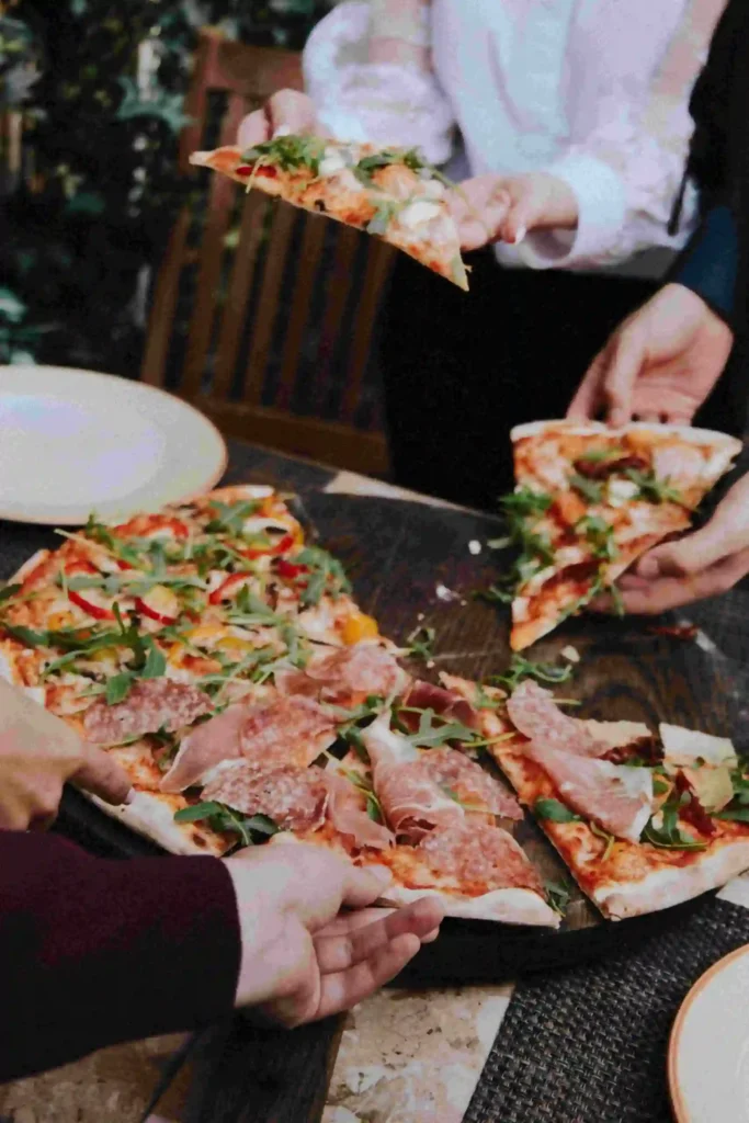 photo d'une pizza avec une part en train d'etre prise par une personne pour la journée de la pizza comme exemple du calendrier des évènements marketing 2025